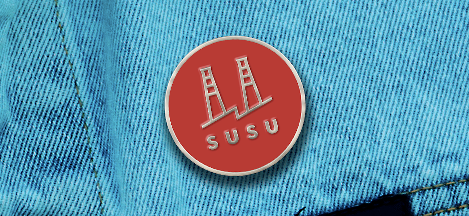 A circular enamel pin in silver and red with the susu logo at the center